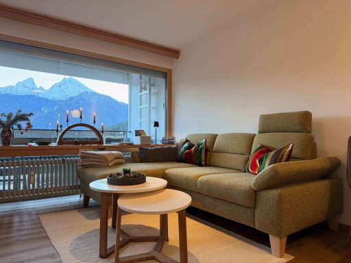 Gemütliches Wohnzimmer mit einem grünen Sofa, Tisch und Blick auf Berge.